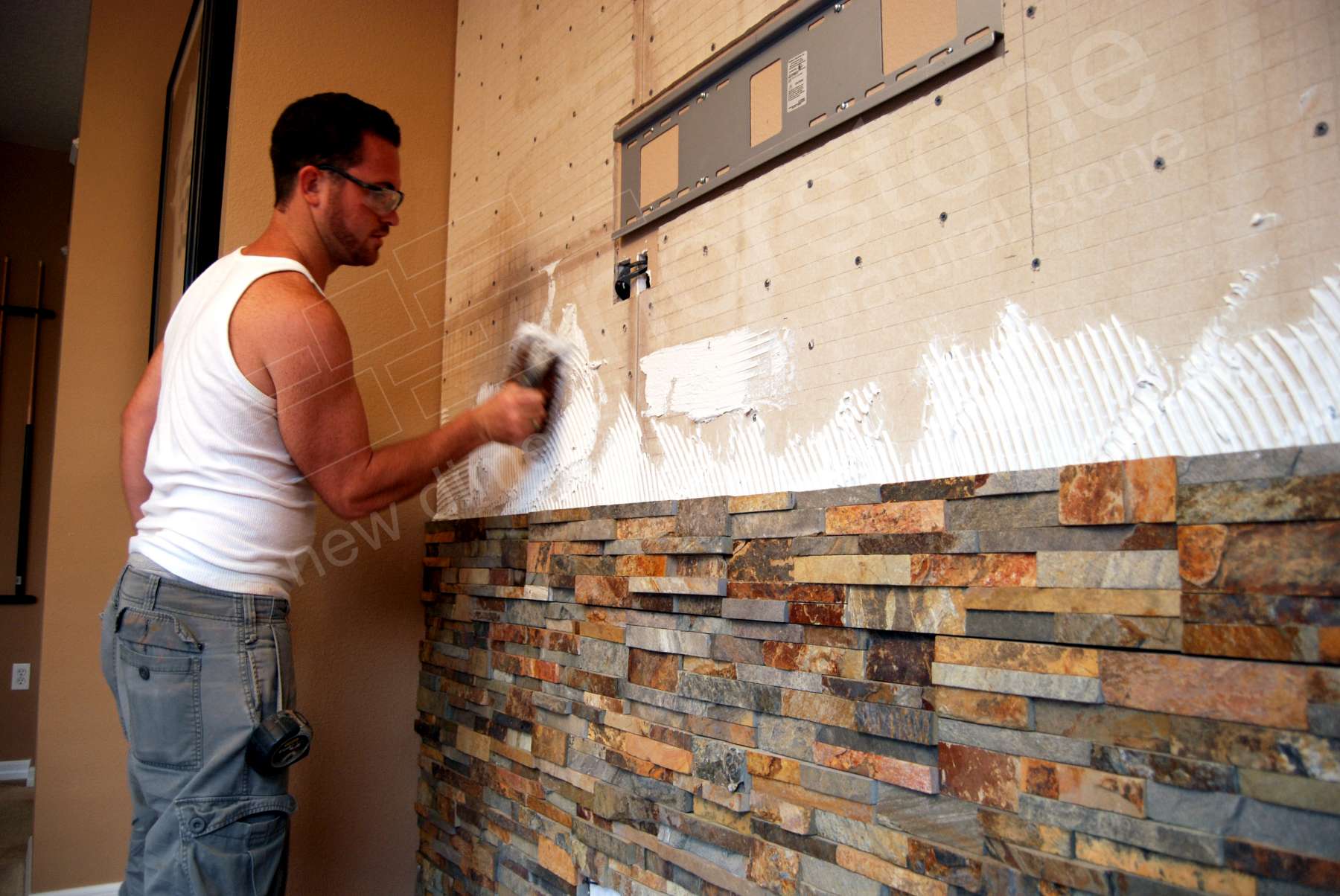 In process installation of stacked stone panels showing thinset coverage on the back of each panel and troweled and notched thinset on the wall